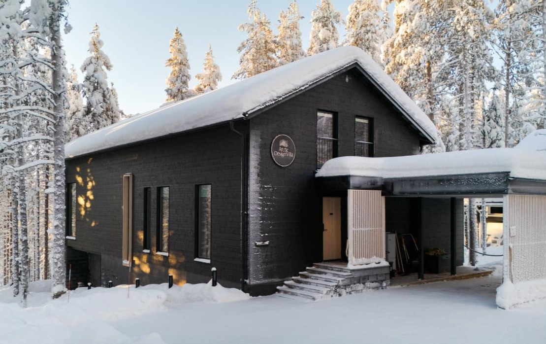 Black-timber design villa at Levi with deep snow on the roof and frosted pines around it